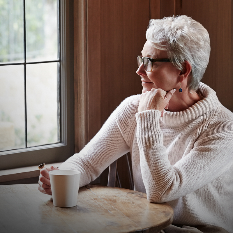 Mature woman contemplates retirement with a coffee by a window.